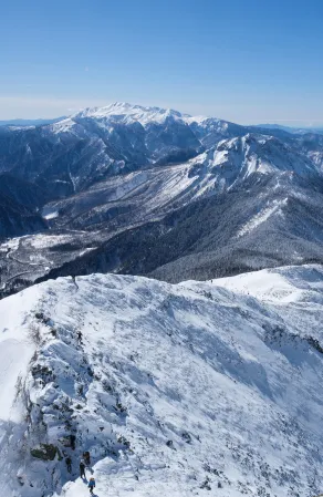 真っ白に染まった雪山を登山する人が見える上空からの景色